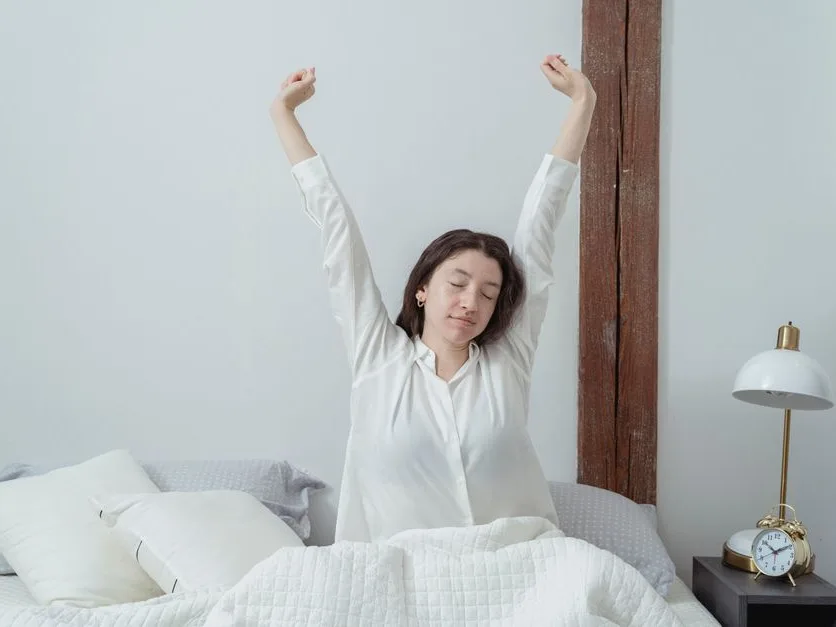 Personne qui s’étire au réveil, assise dans un lit au linge blanc